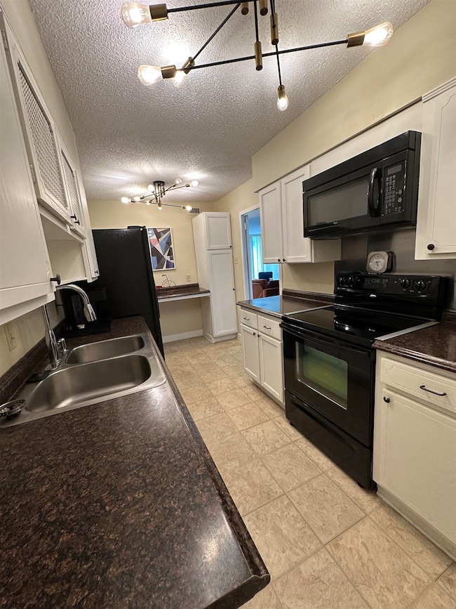 Kitchen with black appliances, white cabinets, a textured ceiling, dark countertops, and light tile patterned flooring
