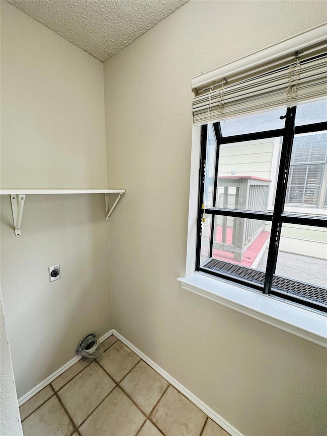 Washroom featuring light tile patterned flooring, a textured ceiling, and electric dryer hookup