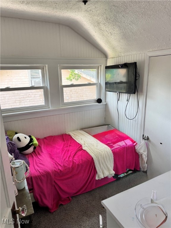 Carpeted bedroom featuring lofted ceiling, a textured ceiling, multiple windows, and wooden walls