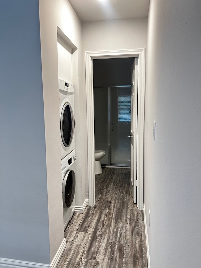 Laundry area featuring dark wood finished floors and stacked washing machine and dryer