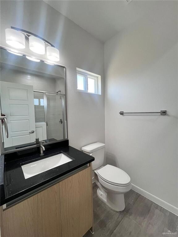 Bathroom featuring vanity, toilet, wood-type flooring, and a shower with door