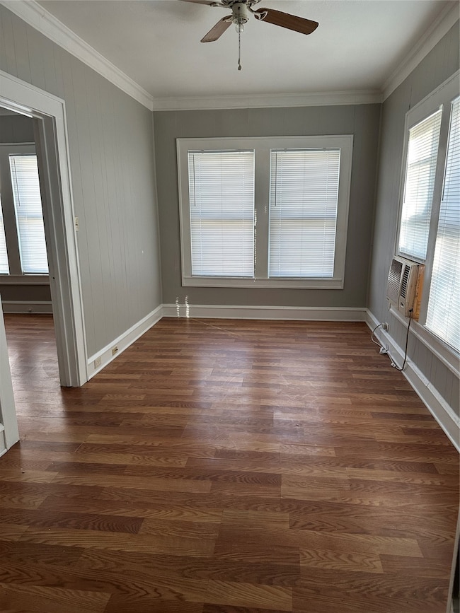 Spare room with ornamental molding, dark wood-type flooring, a ceiling fan, and wooden walls