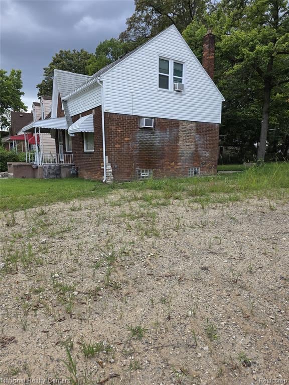 View of side of home with brick siding, a chimney, and a porch