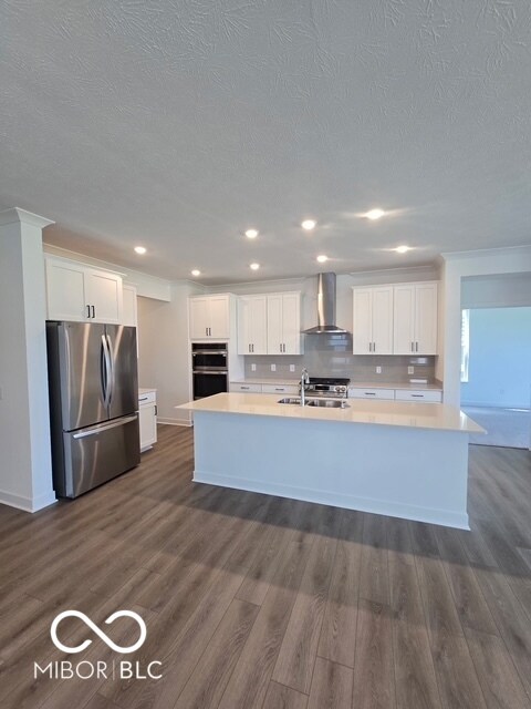 kitchen with stainless steel appliances, white cabinets, a textured ceiling, a kitchen island with sink, and dark wood-style flooring