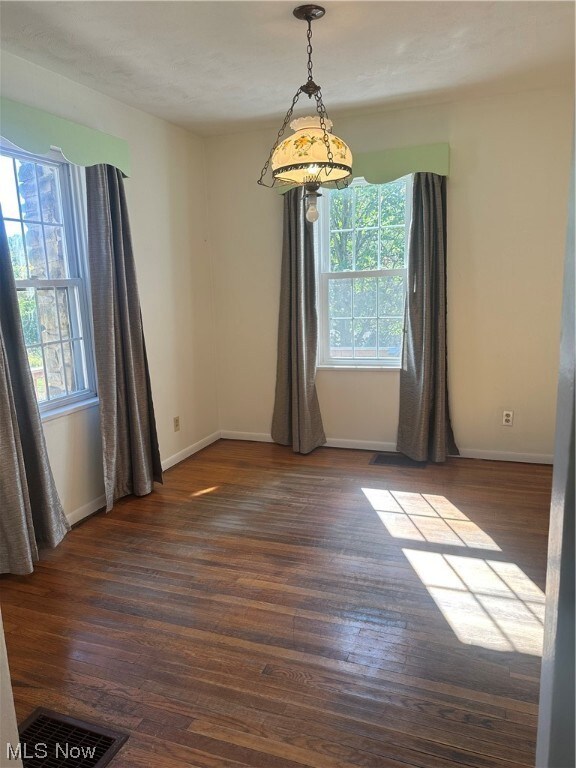 Empty room featuring a healthy amount of sunlight and dark hardwood flooring