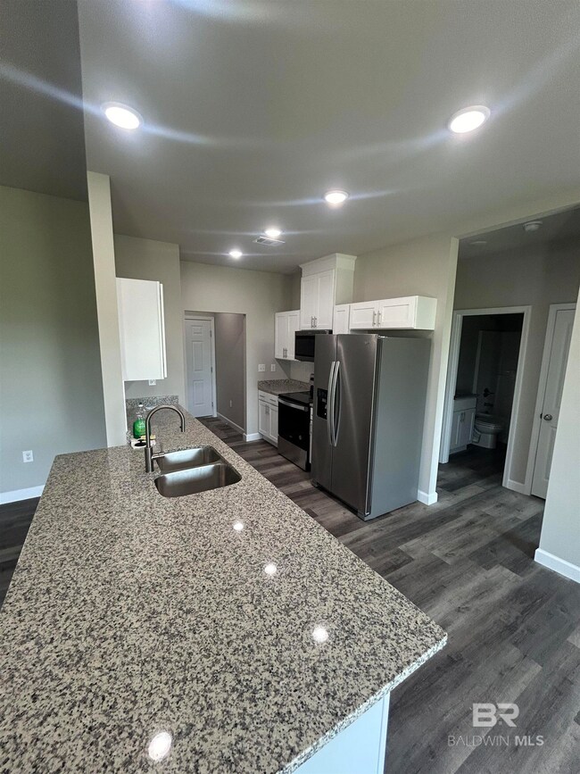Kitchen with appliances with stainless steel finishes, light stone counters, white cabinets, recessed lighting, and dark wood finished floors