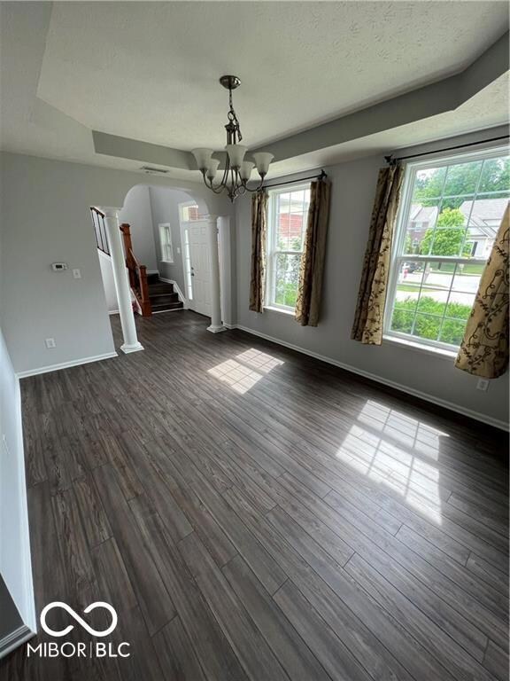unfurnished dining area featuring stairway, baseboards, dark wood finished floors, an inviting chandelier, and arched walkways