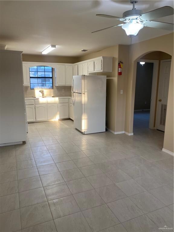 Kitchen featuring a sink, freestanding refrigerator, white cabinetry, arched walkways, and ceiling fan