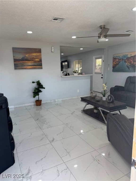 Living area with a textured ceiling, light marble finish flooring, ceiling fan, and recessed lighting