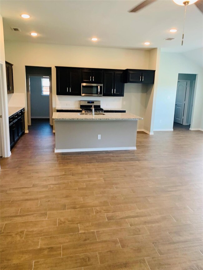 Kitchen with light stone countertops, a kitchen island with sink, sink, light hardwood / wood-style flooring, and appliances with stainless steel finishes