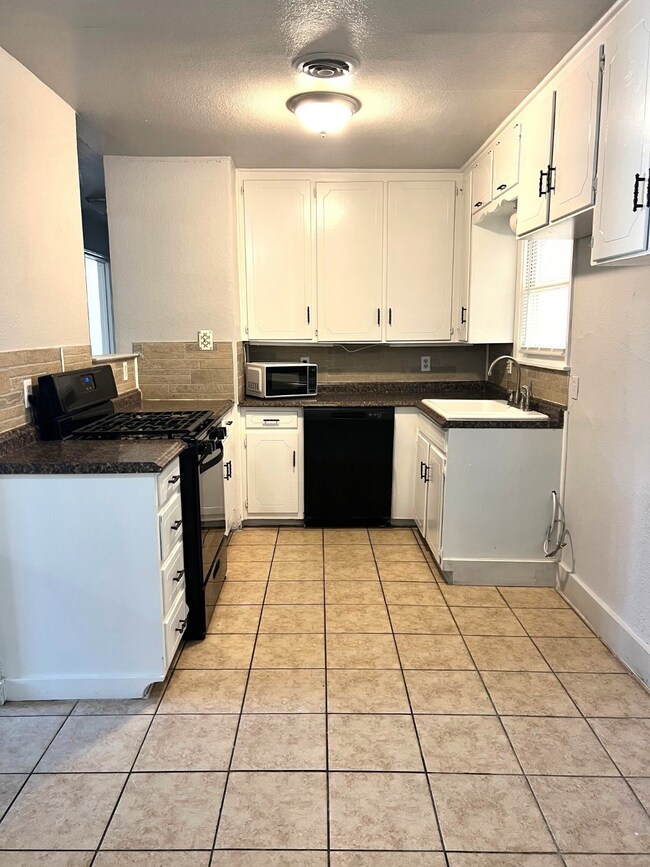 Kitchen featuring black appliances, light tile patterned floors, white cabinets, a textured ceiling, and backsplash