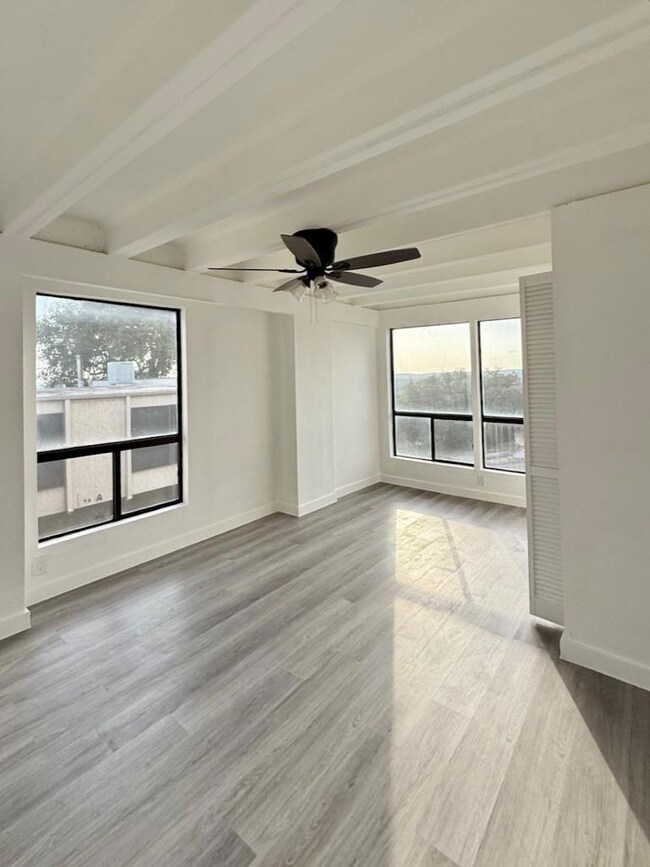 Empty room with beamed ceiling, ceiling fan, and 