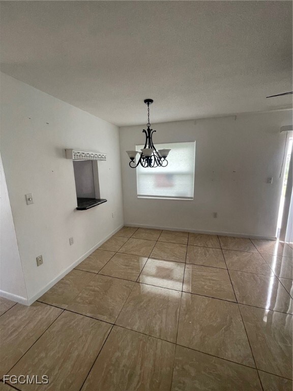 Unfurnished dining area with a chandelier, tile patterned floors, and a textured ceiling