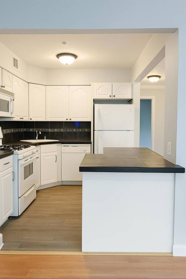 Kitchen featuring white appliances, light wood-type flooring, white cabinetry, and tasteful backsplash