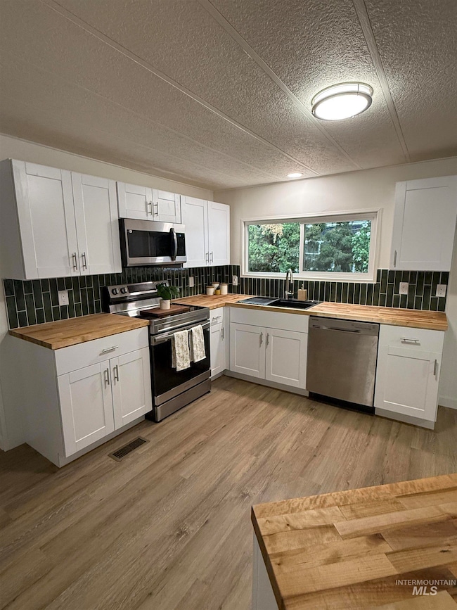 Kitchen featuring butcher block countertops, white cabinetry, stainless steel appliances, tasteful backsplash, and a textured ceiling