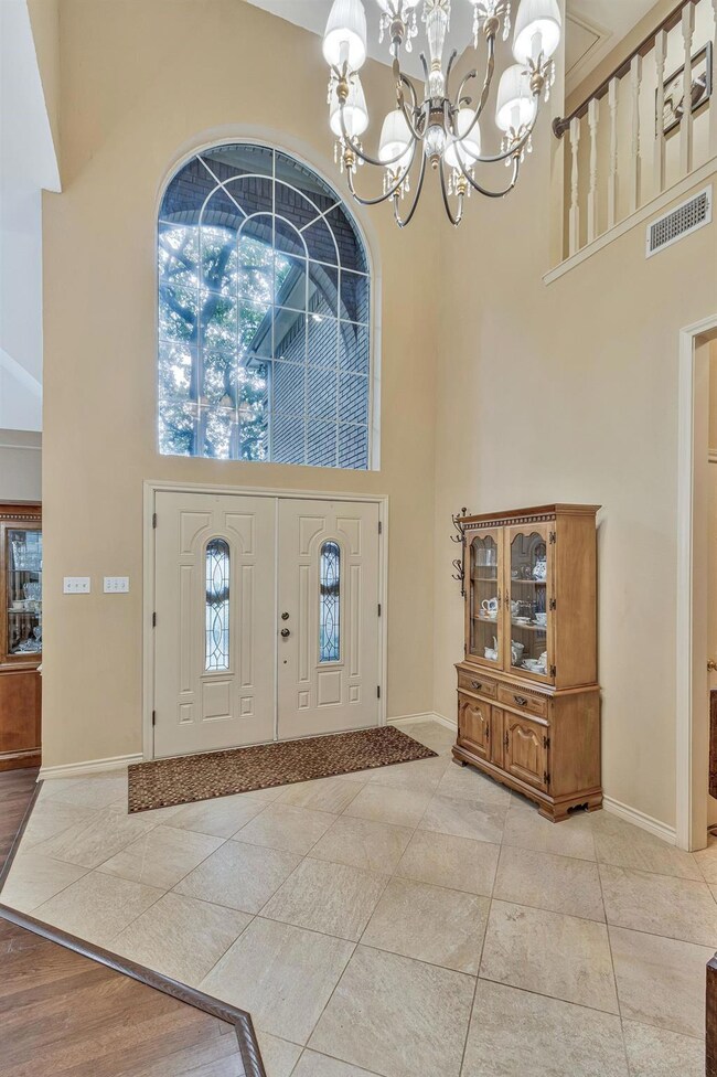 Foyer with a healthy amount of sunlight, a towering ceiling, light tile flooring, and a notable chandelier