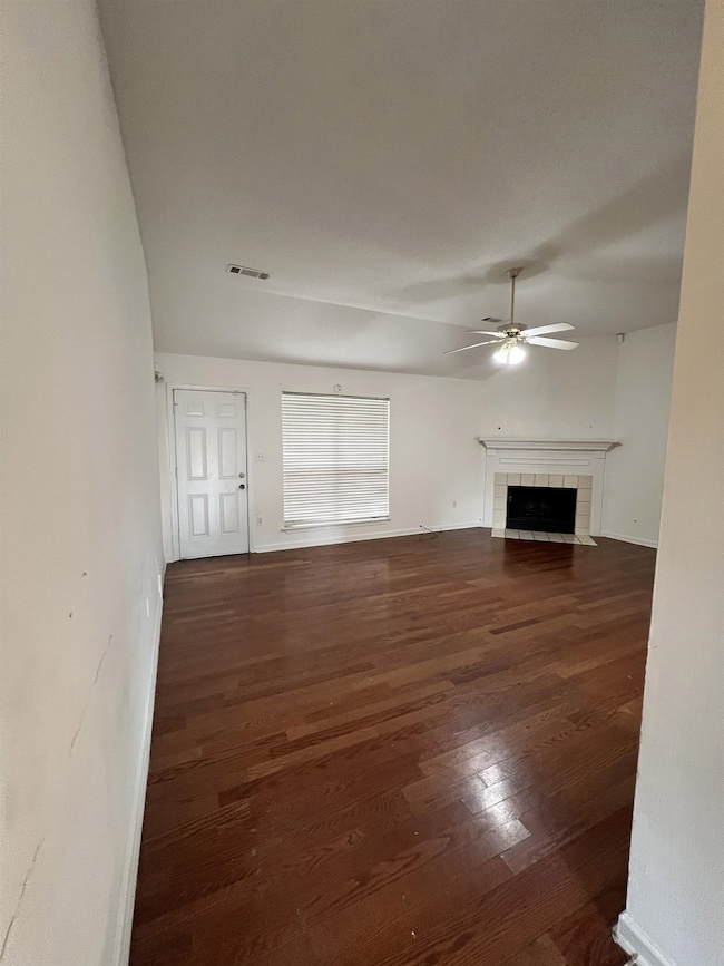Unfurnished living room featuring a tiled fireplace, dark wood finished floors, and ceiling fan