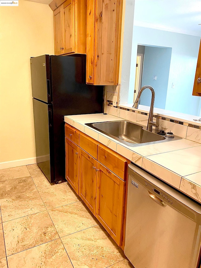 Kitchen with dishwasher, a sink, tile countertops, baseboards, and freestanding refrigerator