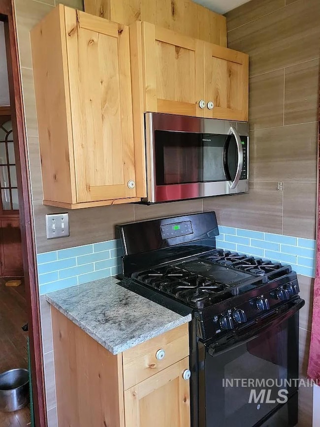 Kitchen with black range with gas cooktop, stainless steel microwave, light brown cabinets, and decorative backsplash