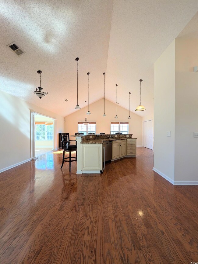 Kitchen with open floor plan, decorative light fixtures, lofted ceiling, dark wood-style flooring, and a breakfast bar area