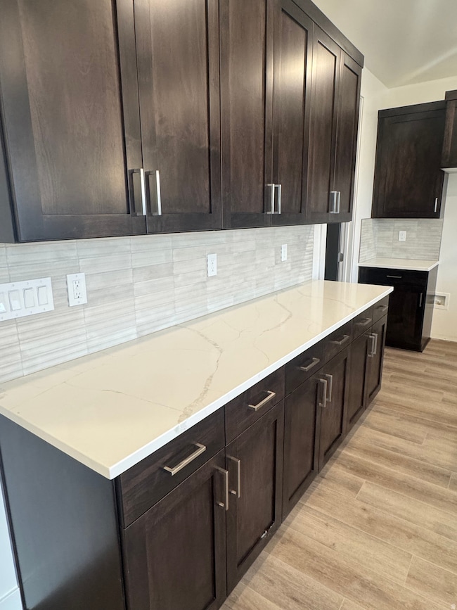 Kitchen featuring tasteful backsplash, dark brown cabinetry, light wood finished floors, and light stone countertops