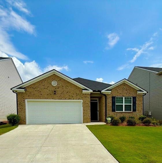 Single story home featuring an attached garage, brick siding, driveway, and a front yard