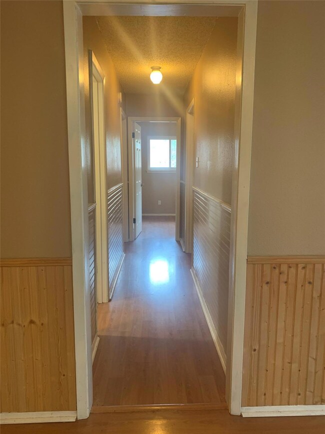 Hall with wood finished floors, a wainscoted wall, a textured ceiling, and wooden walls