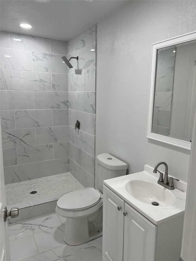 Bathroom featuring a stall shower, light marble finish flooring, vanity, a textured wall, and recessed lighting
