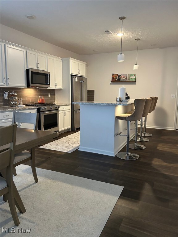 Kitchen featuring a kitchen bar, white cabinets, stainless steel appliances, and tasteful backsplash
