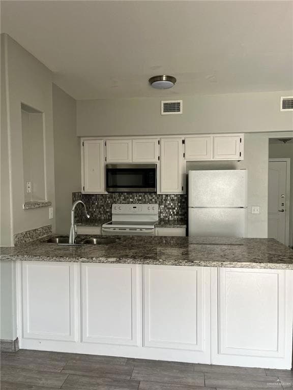Kitchen featuring white appliances, white cabinets, backsplash, and a peninsula