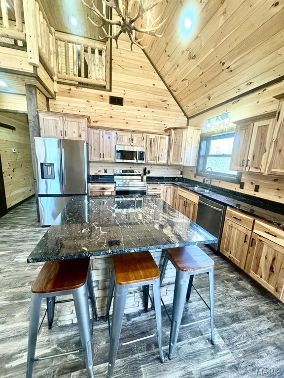 Kitchen featuring dark wood-type flooring, light brown cabinets, appliances with stainless steel finishes, dark stone countertops, and wood ceiling