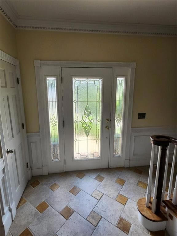 Foyer entrance with stone tile flooring, wainscoting, a decorative wall, ornamental molding, and plenty of natural light