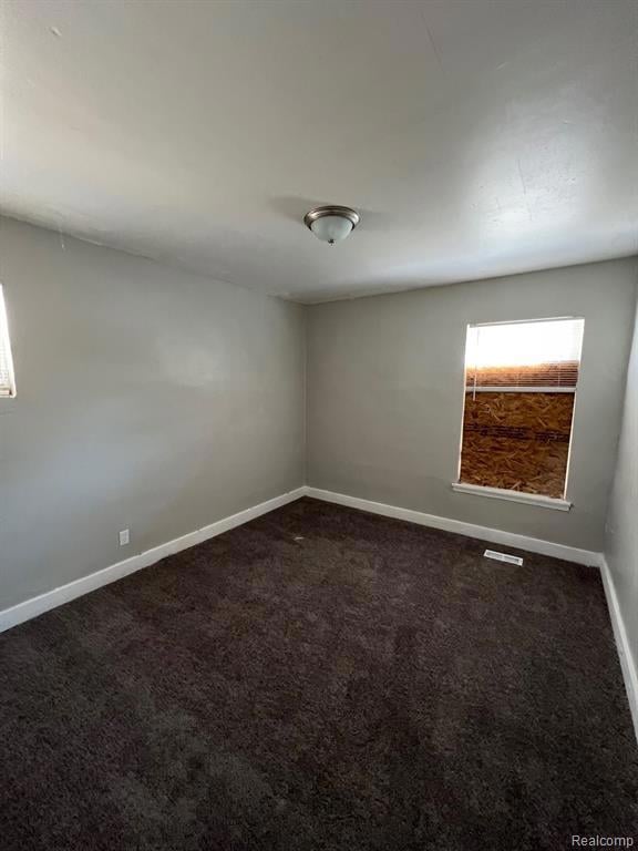 Unfurnished room featuring dark colored carpet and baseboards