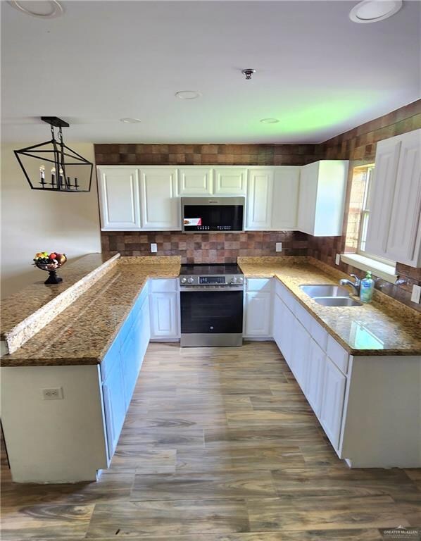 Kitchen with stainless steel appliances, white cabinets, a peninsula, tasteful backsplash, and hanging light fixtures