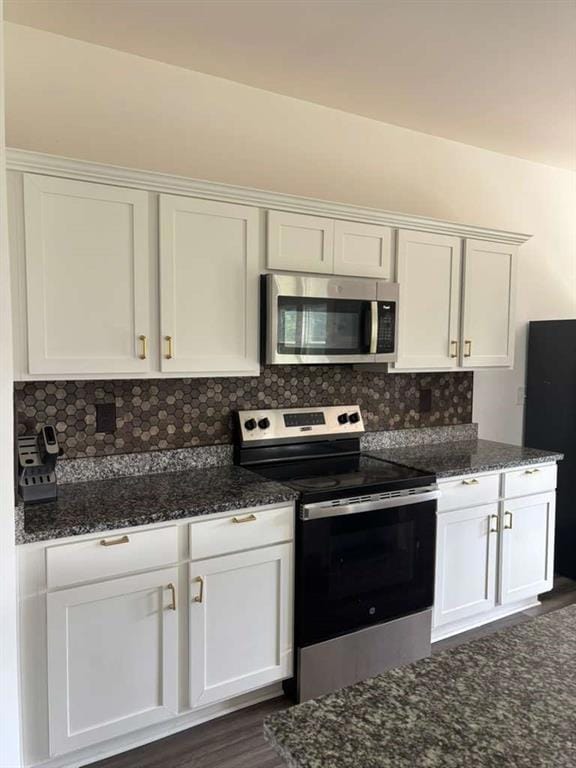 Kitchen featuring appliances with stainless steel finishes, backsplash, white cabinets, and dark stone counters