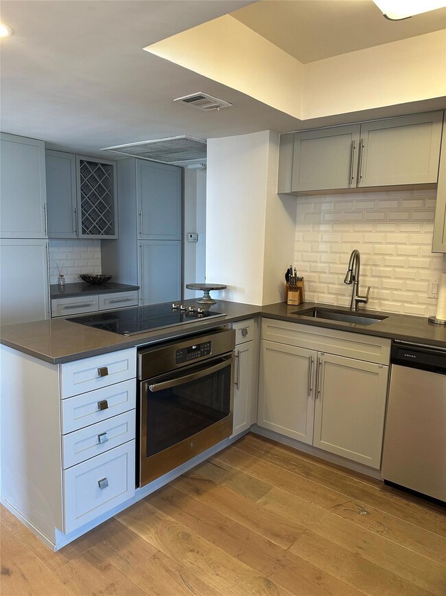 Kitchen featuring decorative backsplash, appliances with stainless steel finishes, a peninsula, and light wood finished floors