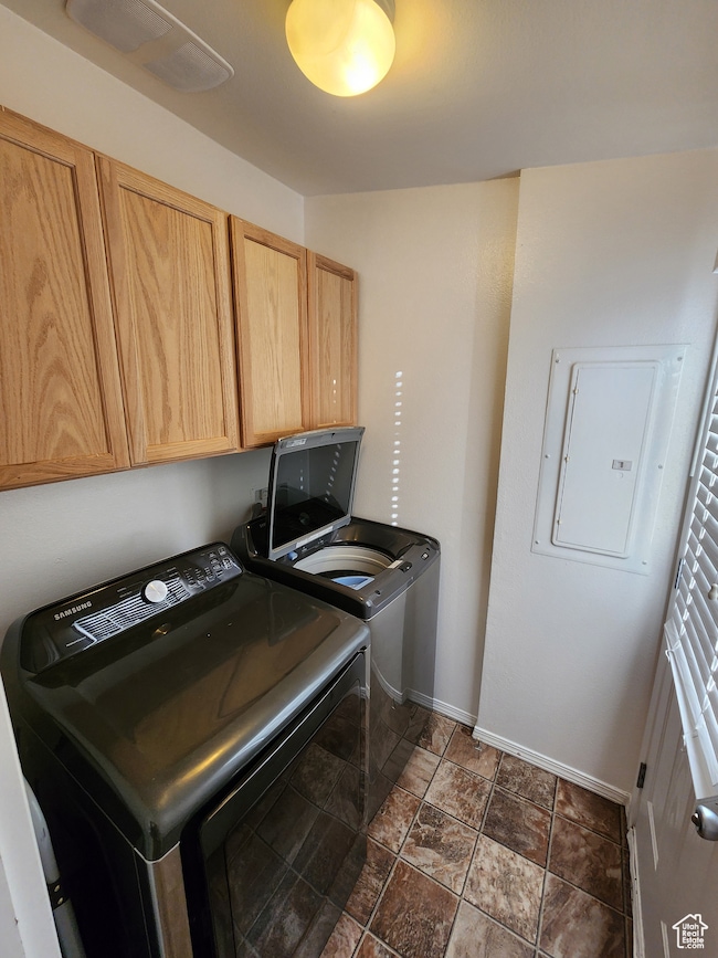 Laundry room featuring independent washer and dryer, cabinet space, dark stone finish floors, and electric panel