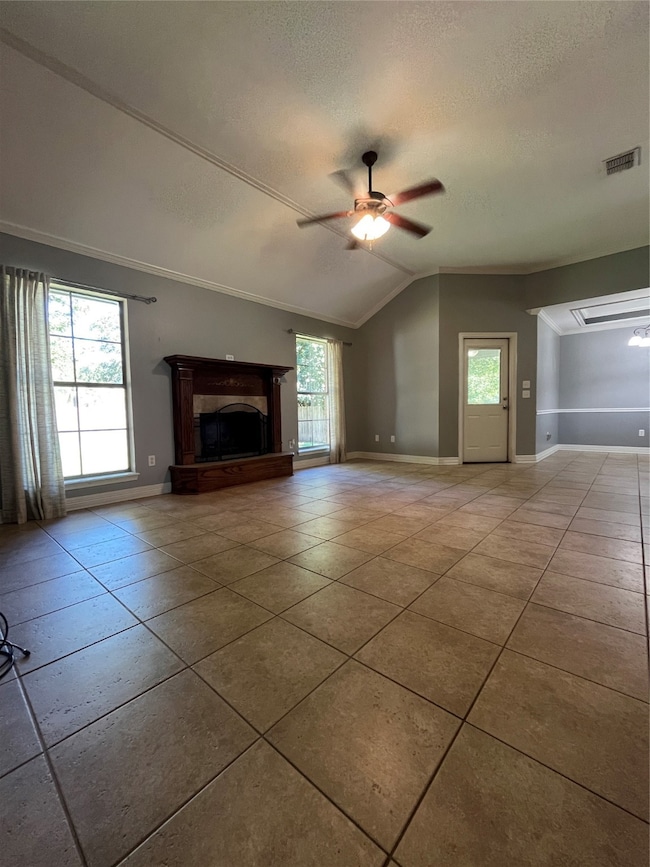 Unfurnished living room featuring a ceiling fan, a fireplace with raised hearth, a textured ceiling, vaulted ceiling, and ornamental molding