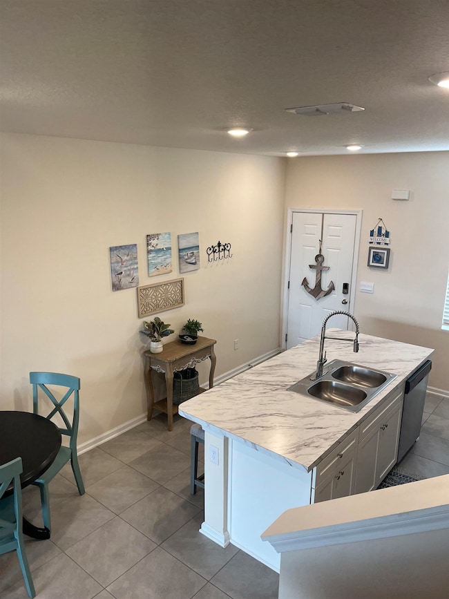 Kitchen featuring light countertops, light tile patterned floors, stainless steel dishwasher, a kitchen island with sink, and white cabinets
