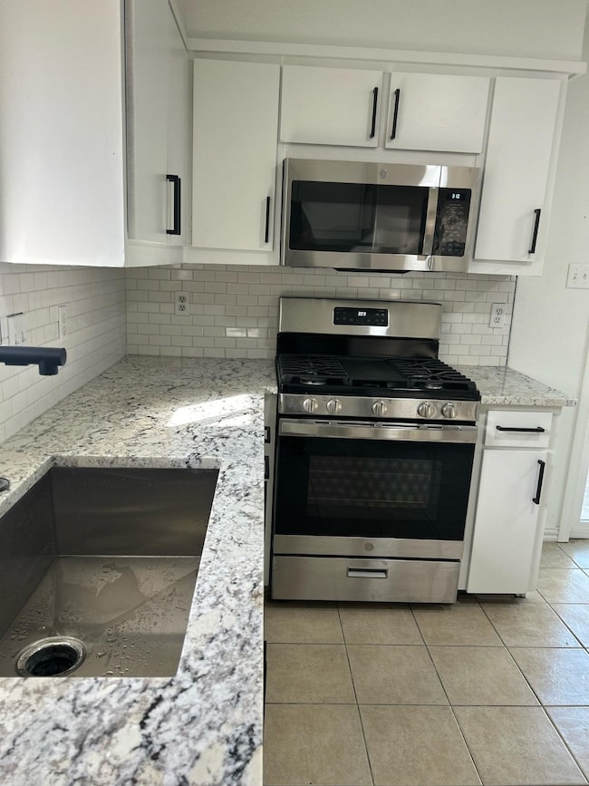 Kitchen featuring appliances with stainless steel finishes, white cabinets, backsplash, and light tile patterned floors