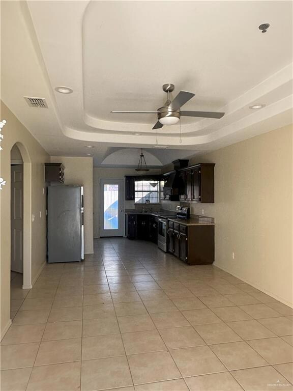 Kitchen featuring appliances with stainless steel finishes, a tray ceiling, ceiling fan, and light tile patterned flooring