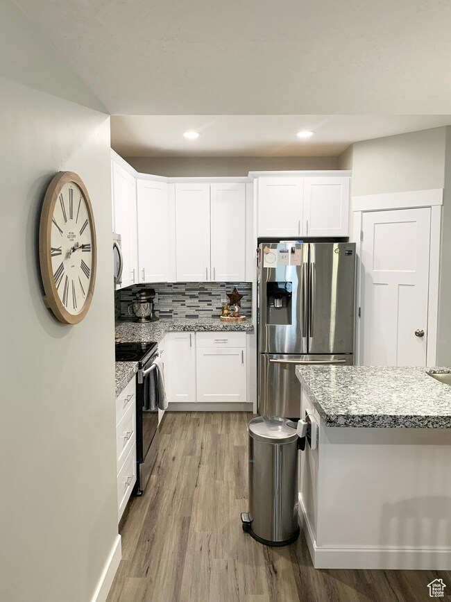 Kitchen with stainless steel appliances, backsplash, light stone countertops, white cabinets, and recessed lighting