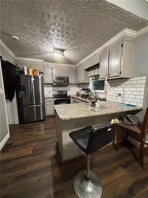 Kitchen with crown molding, appliances with stainless steel finishes, a peninsula, a kitchen breakfast bar, and dark wood-style floors