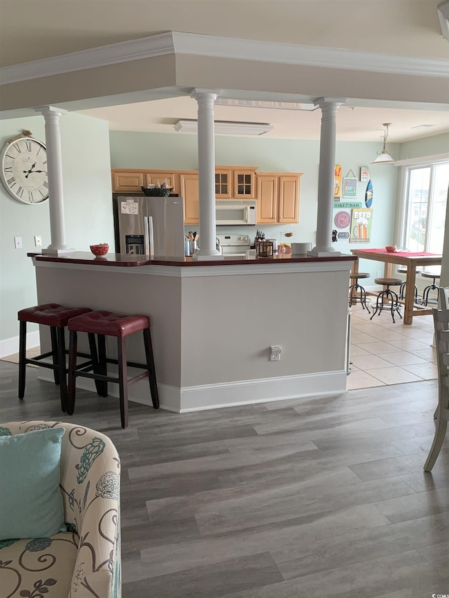 Kitchen with decorative columns, pendant lighting, light brown cabinets, and white appliances