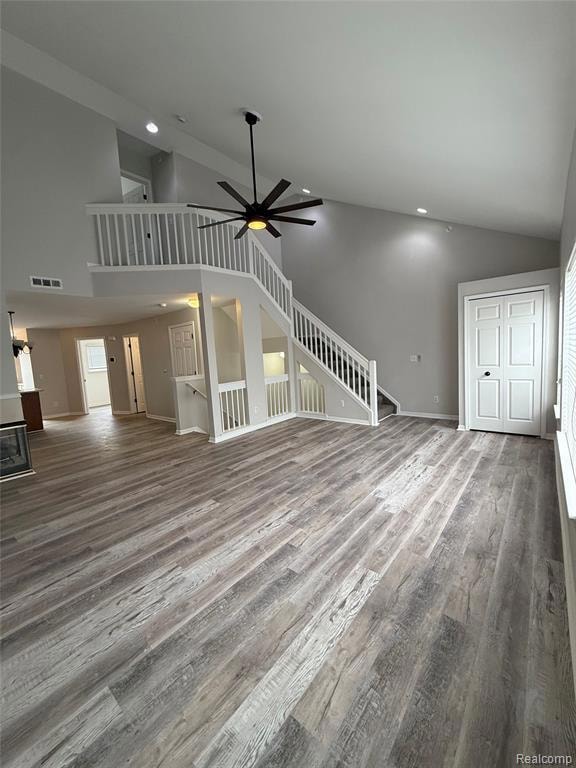 Unfurnished living room featuring high vaulted ceiling, stairs, wood finished floors, a ceiling fan, and recessed lighting