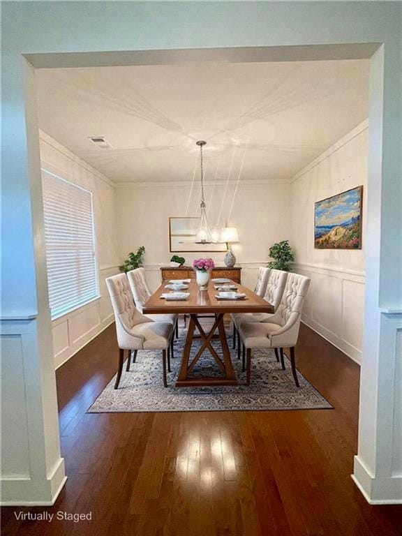 Dining space featuring wood finished floors, a decorative wall, ornamental molding, and wainscoting