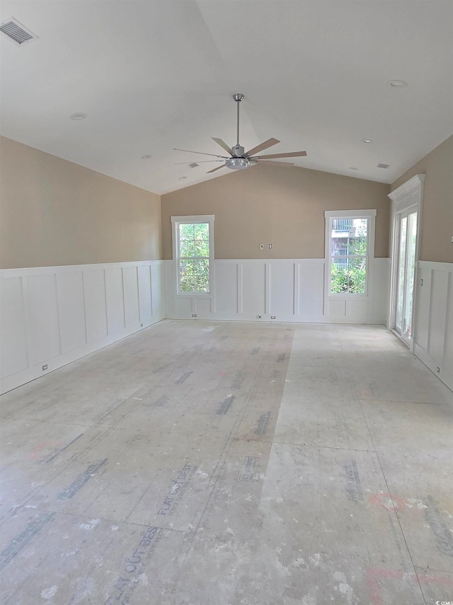 Unfurnished room featuring a ceiling fan, visible vents, wainscoting, and lofted ceiling