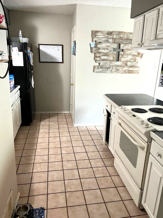 Kitchen with electric stove, white cabinetry, light tile flooring