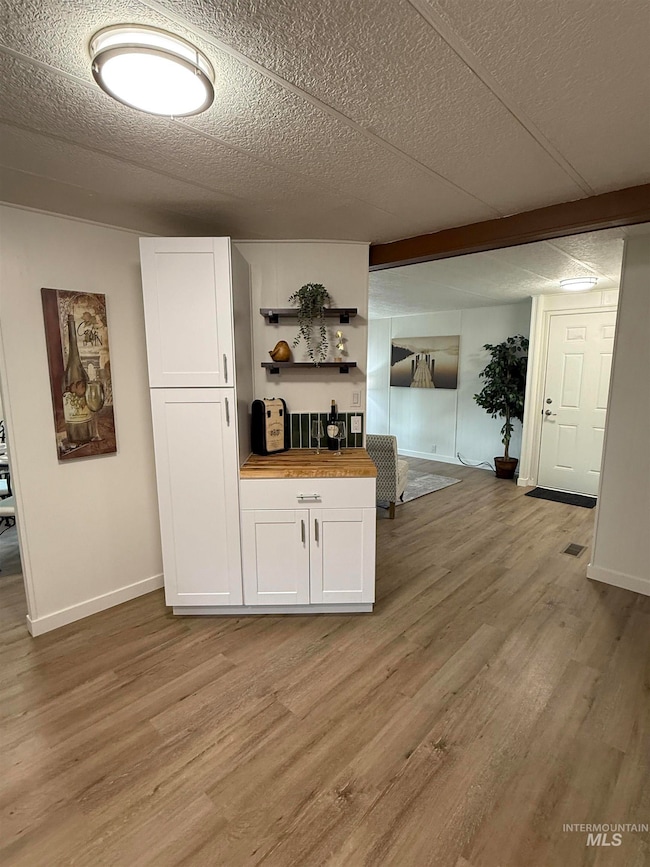 Bar featuring open shelves, white cabinets, butcher block countertops, light wood-type flooring, and a textured ceiling