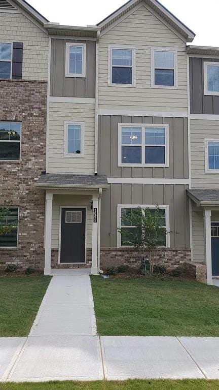 View of front of property featuring board and batten siding, a front yard, and brick siding